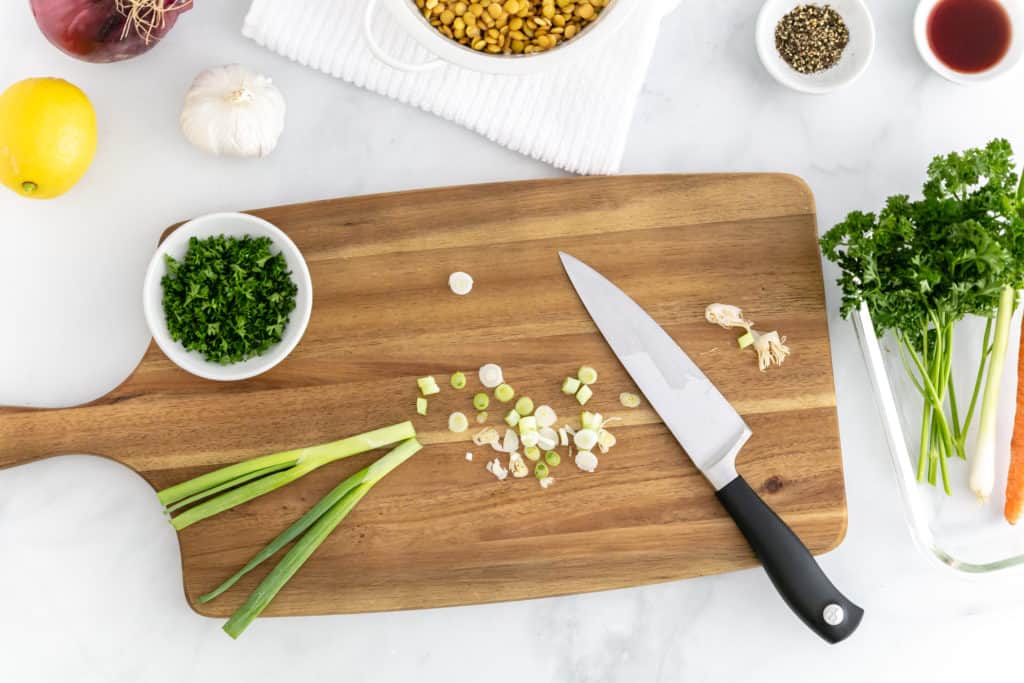 Overhead image of some of the salad ingredients including parsley, lentils and  lemon, with green onion chopped on the cutting board.