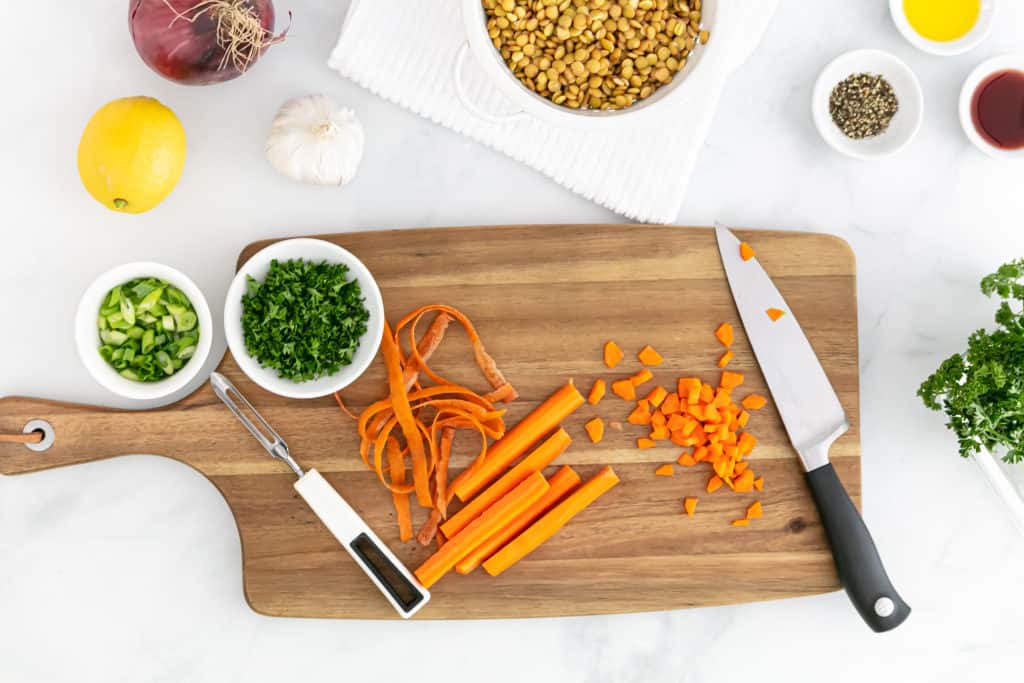 Overhead image of some of the salad ingredients including parsley, lentils and  lemon, with carrots chopped on the cutting board.