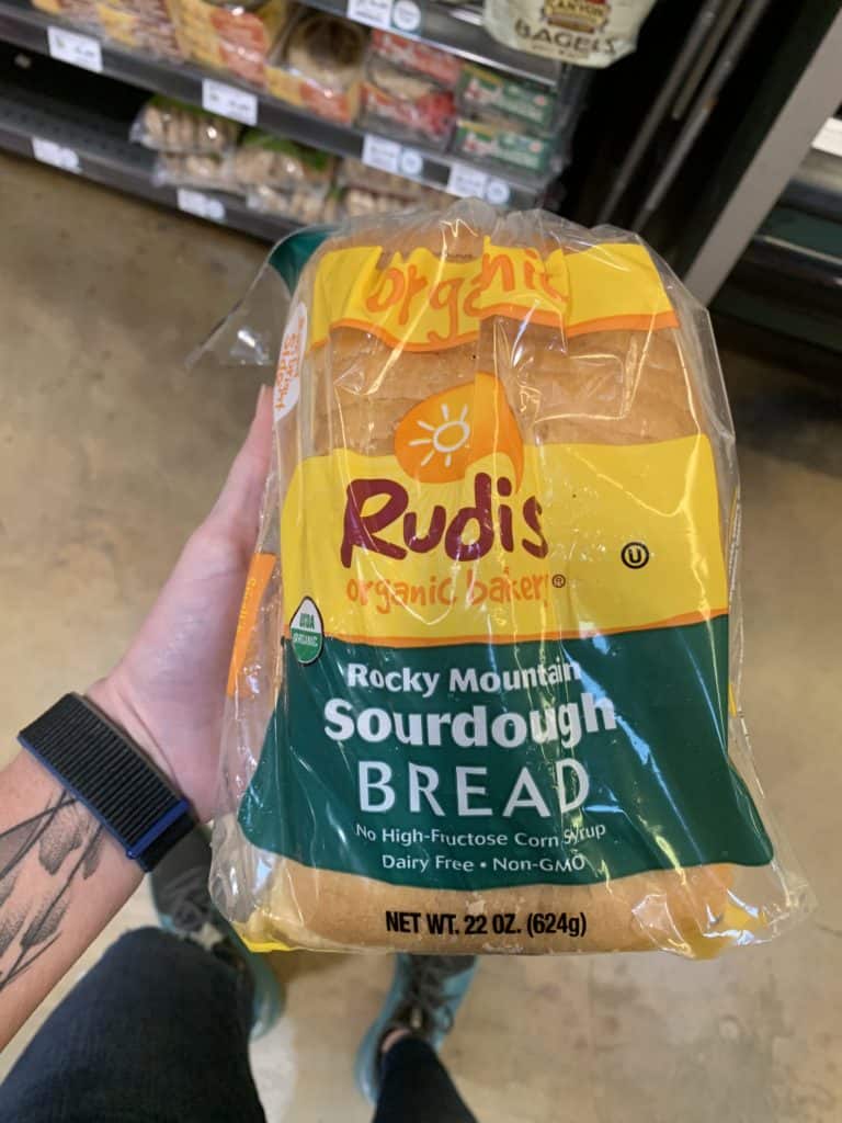 Close up image of a hand holding a loaf of Rudis Bread with a clear and yellow/green label.