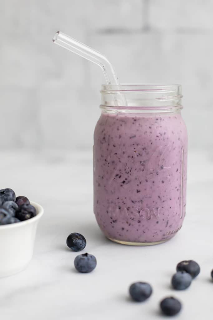 Close up side view of a mason jar filled with the Blueberry Protein Smoothie, with blueberries in a bowl beside it.