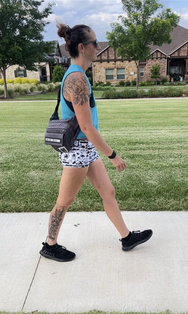 Image of Lacey walking in shorts and a tank top, carrying a side pack
