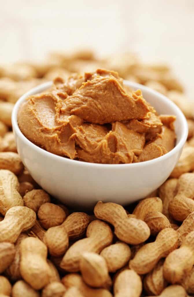 peanut butter in a bowl surrounded by peanuts in there shells