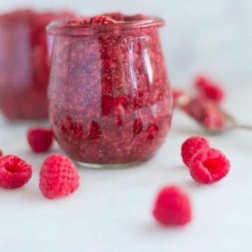 side view of raspberry chia jam in a jar with raspberries next to it.
