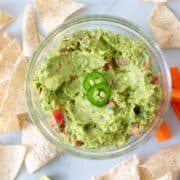 Top down view of perfect guacamole in a bowl with some jalapeños on top.