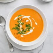 White bowl of creamy sweet potato soup garnished with cilantro, a drizzle of coconut milk, and freshly ground pepper.