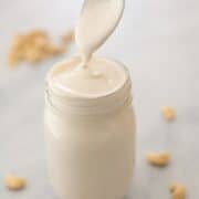 Side top view of Cashew Sauce in a jar with cashews on next to it.
