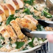 Top angled view of finished Chicken Florentine in a pan being picked up with tongs.